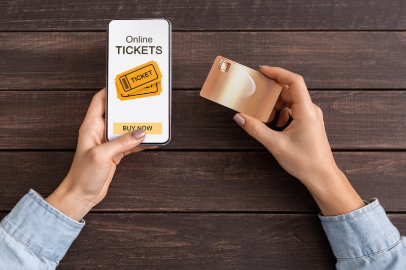 Frau nutzt Smartphone zum Kauf von Online-Tickets, Bankkarte in der Hand.