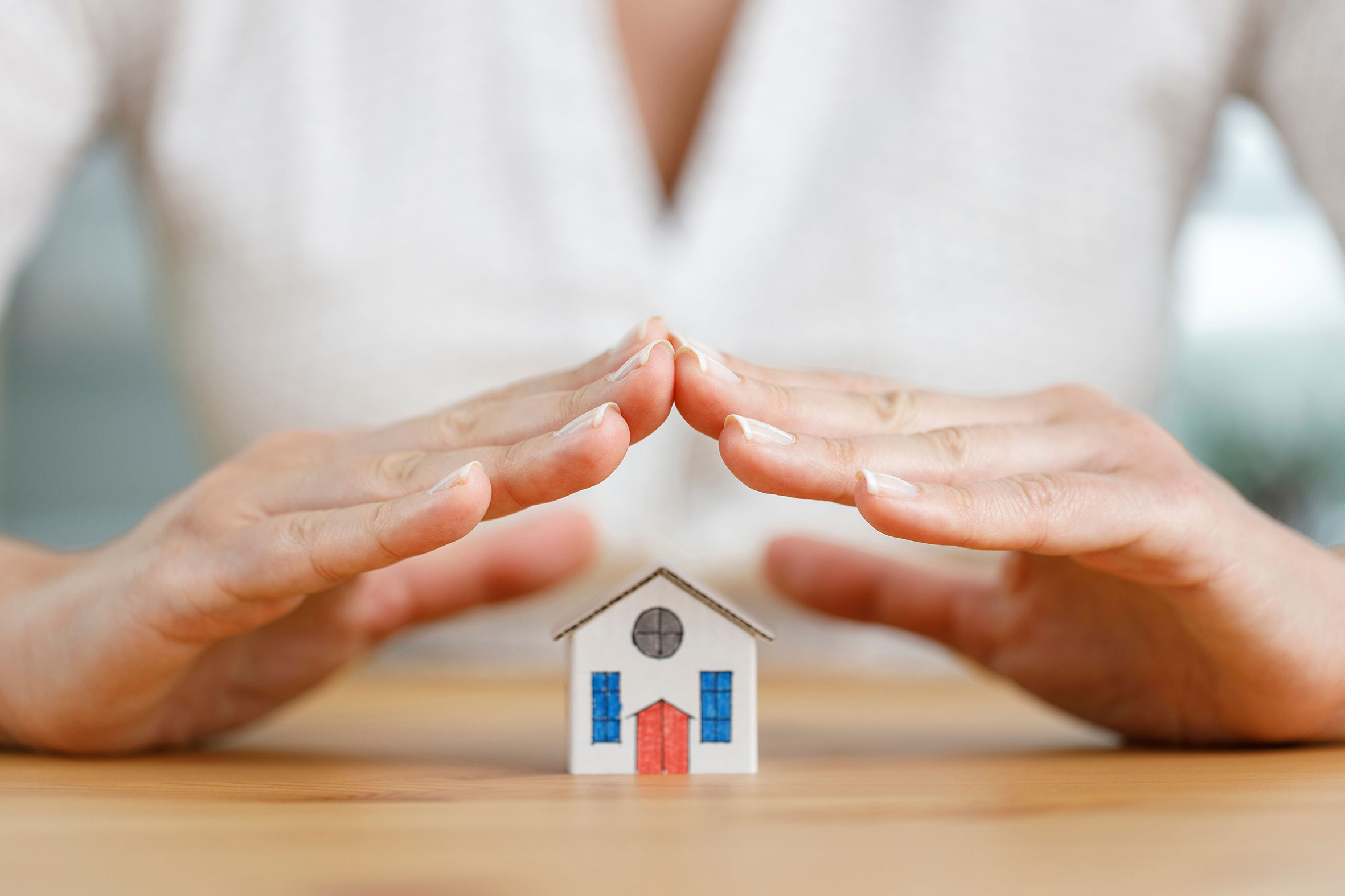 Zwei Hände werden schützend über ein kleines Papphaus gehalten.